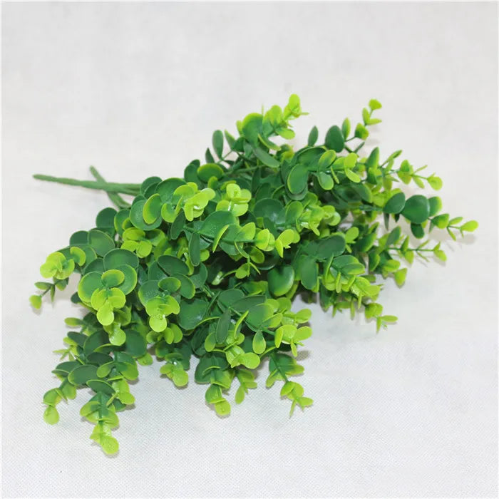 A cluster of artificial eucalyptus stems with small, rounded, bright and dark green leaves on a white background.