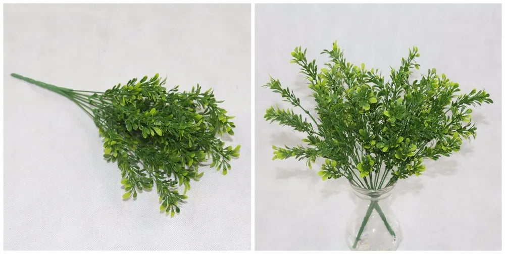 Artificial green fern-like grass stems with layered leaves, shown lying flat and arranged in a clear glass vase.