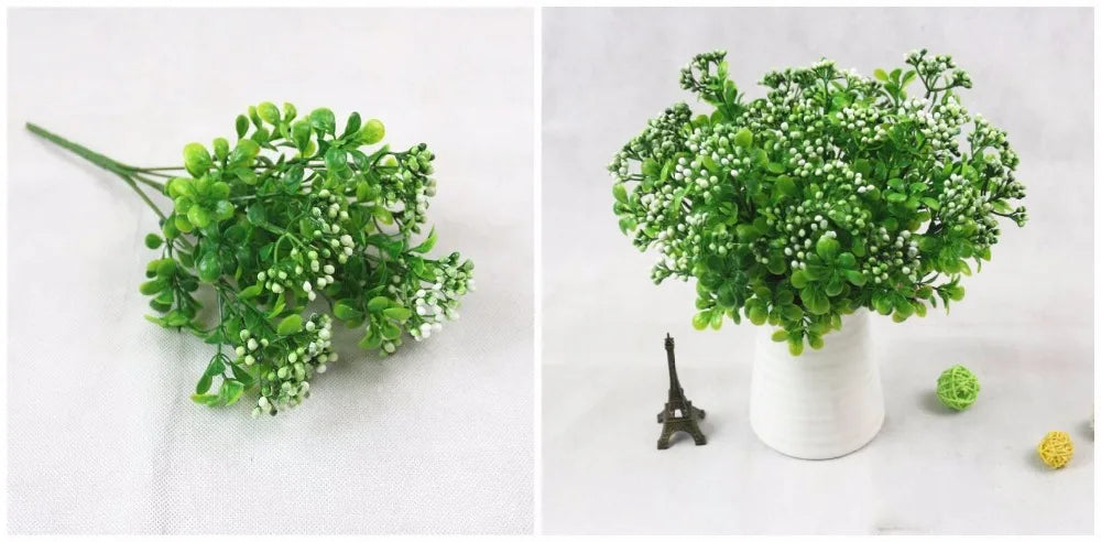 Artificial green leaf plant with small white flowers, shown as a loose stem and arranged in a white ceramic vase.