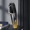 Black and gold cordless hair trimmer with a T-blade and digital display, standing upright on a table.