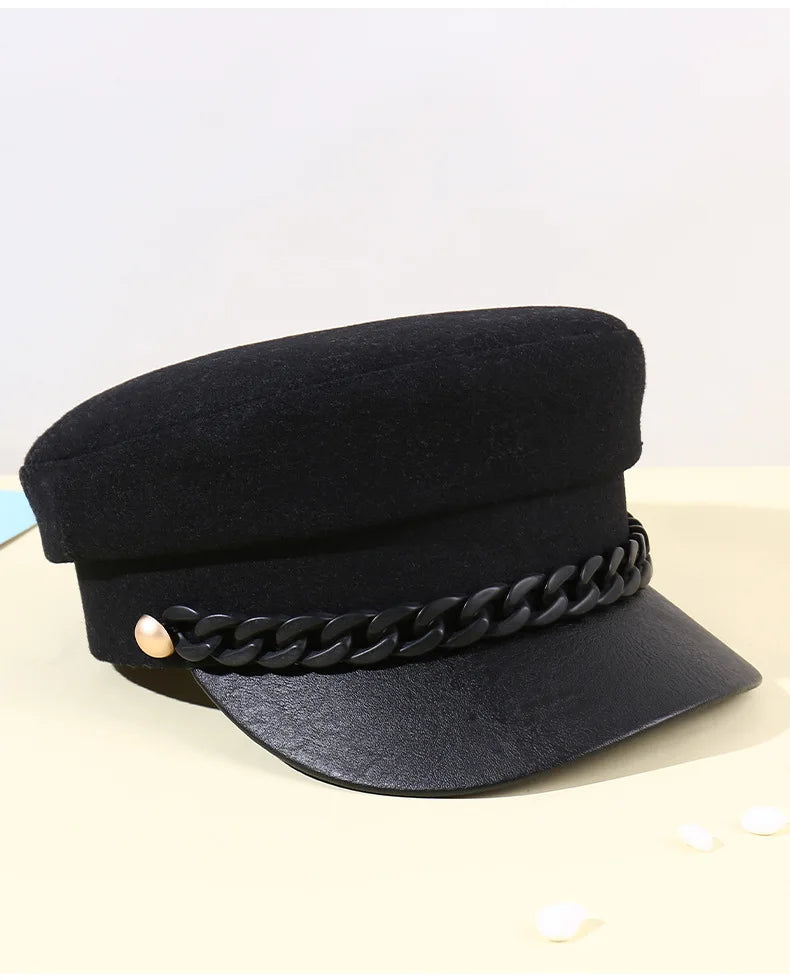 Black felt baker boy hat with a faux leather peak, decorative black chain trim and gold-tone side detail.