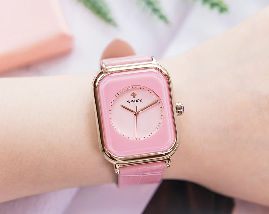 Ladies' square watch featuring a pink dial, polished gold-tone case and a textured pink leather strap on a wrist.
