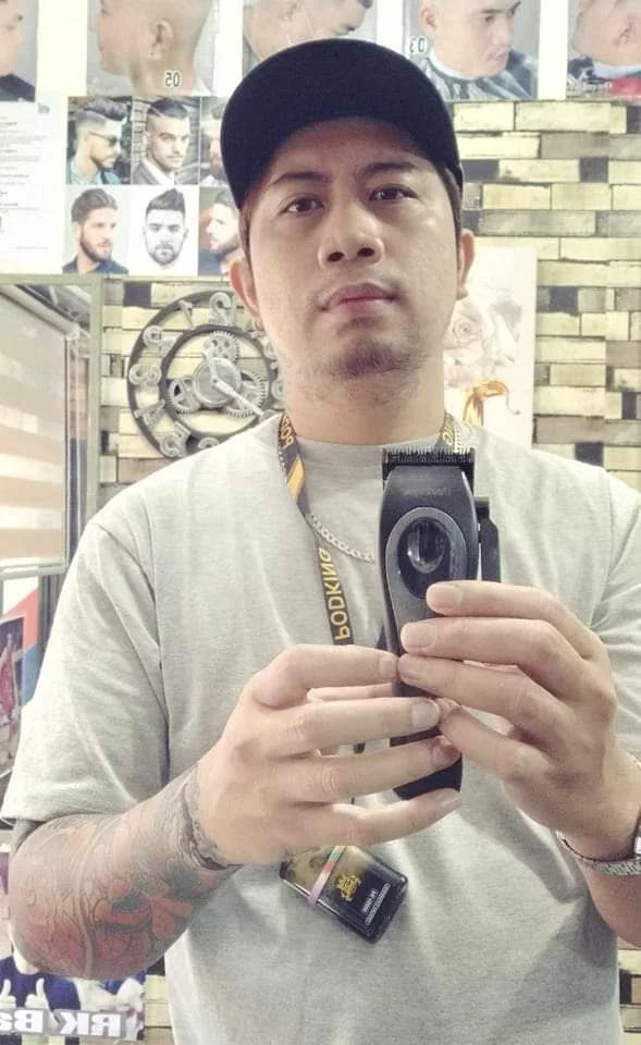 Man in a barbershop holding a sleek, black professional cordless hair clipper and grooming trimmer.