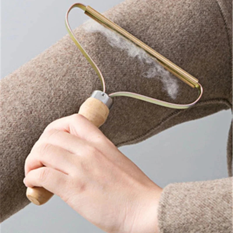 Hand holding a wooden-handled metal lint remover, clearing bobbles from a beige wool jumper.