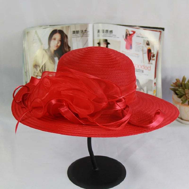 Vibrant red wide-brim occasion hat featuring a decorative organza floral accent, displayed on a stand.