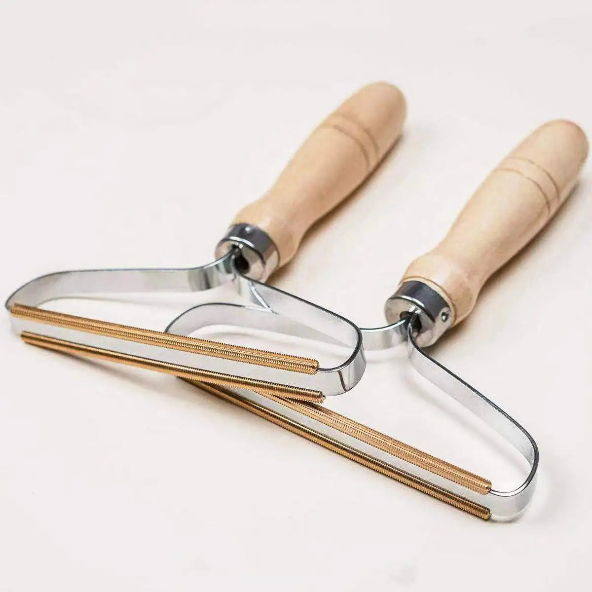 Two metal lint removers with wooden handles and gold-toned wire cleaning edges, angled on a white surface.