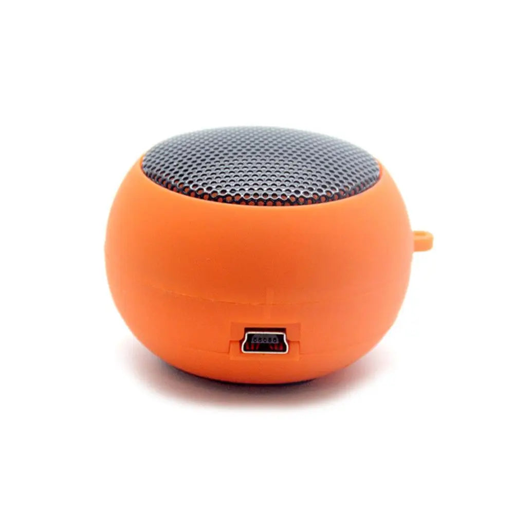 Small, round, orange portable wireless speaker with a metallic silver mesh top and a micro-USB charging port.