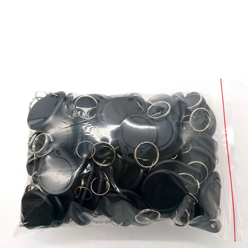Bulk pack of round black plastic RFID key fob tags with metal split rings inside a clear plastic bag.
