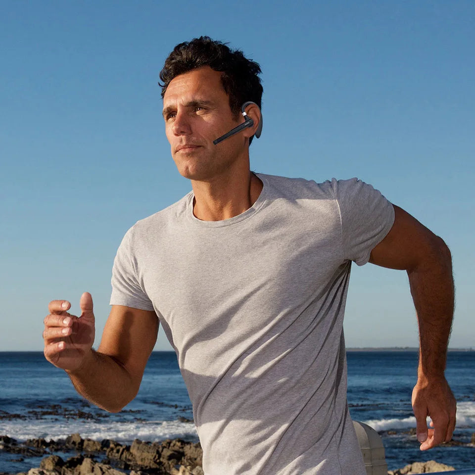 A man running by the sea wearing a sleek, black wireless Bluetooth earpiece with a built-in microphone.