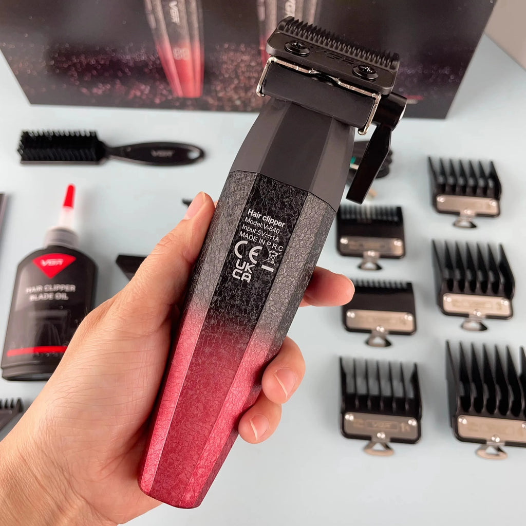 A hand holds a cordless hair and beard trimmer with a black-to-red ombre, textured finish and included guide combs.
