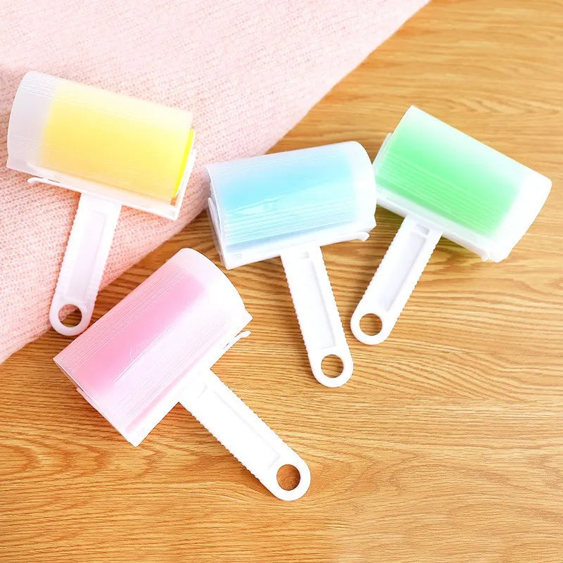 Four reusable lint rollers with white handles and yellow, blue, green, and pink sticky rollers on a wooden surface.