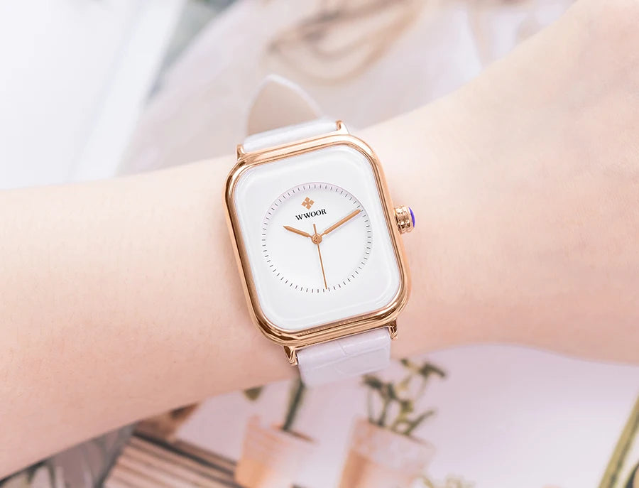 Ladies’ square watch with a white dial, rose gold case, and a pale lilac leather strap worn on a wrist.