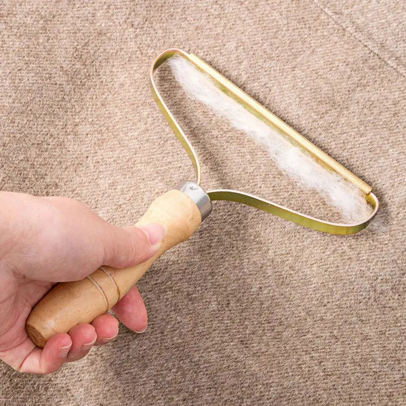 Hand holding a portable fabric lint remover with a wooden handle and a metal gold-coloured blade.