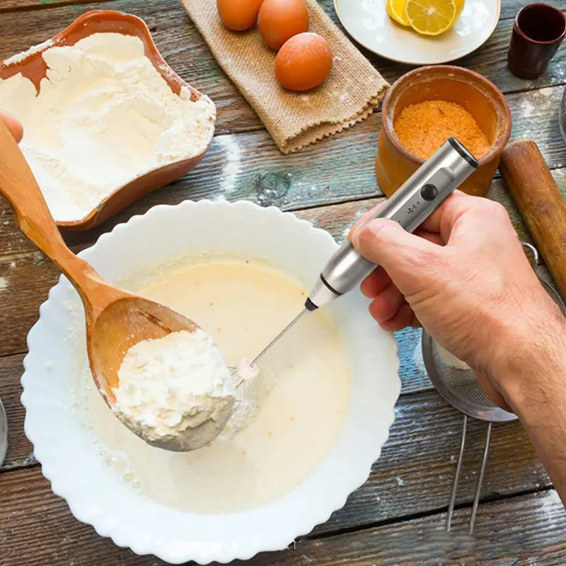 Handheld silver electric milk frother and whisk being used to mix batter in a white bowl.