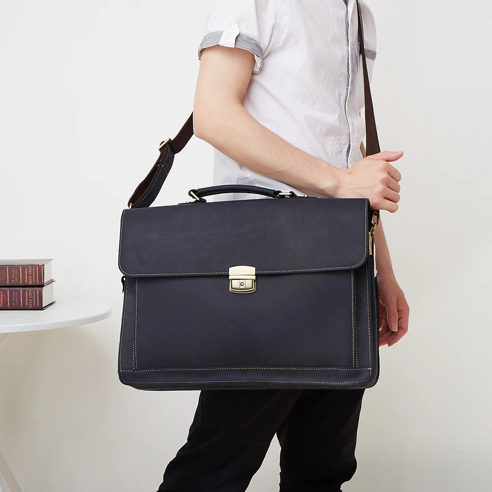 A man carrying a sleek, navy-blue leather laptop briefcase with a top handle, adjustable strap and gold-tone clasp.