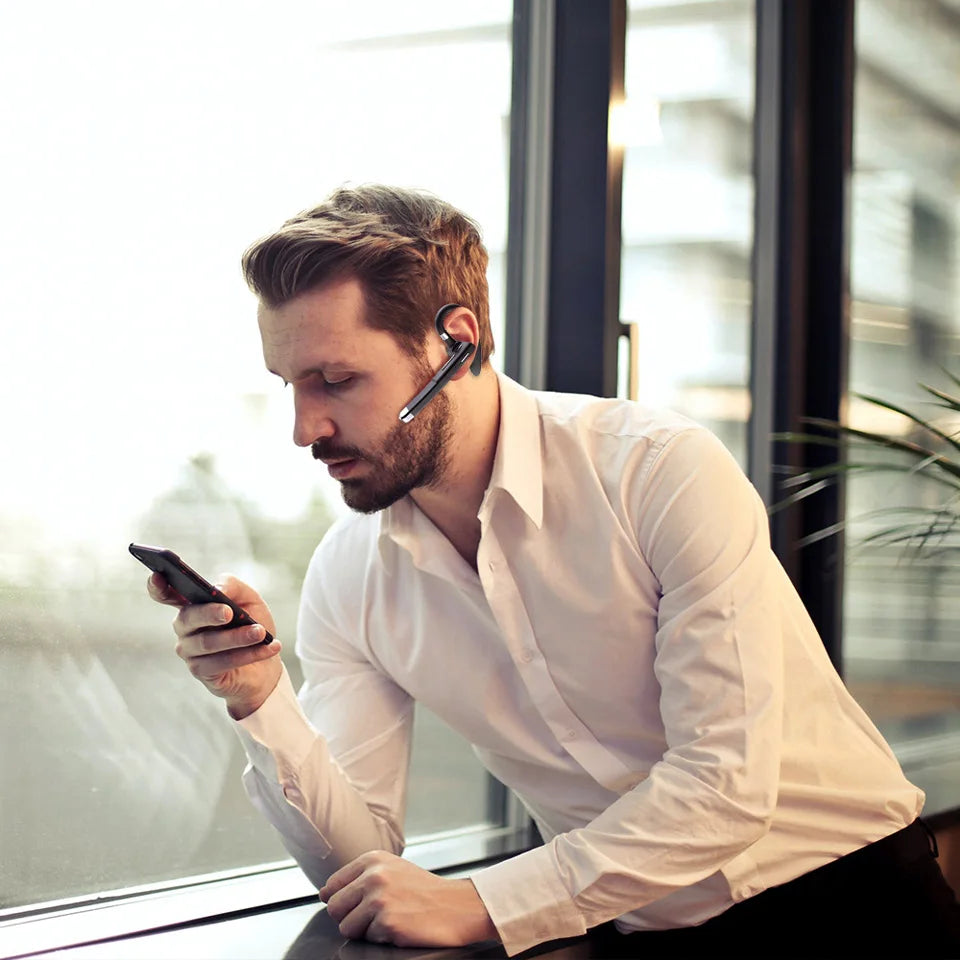 Man in a white shirt wearing a sleek, black wireless Bluetooth earpiece with a microphone while looking at his phone.