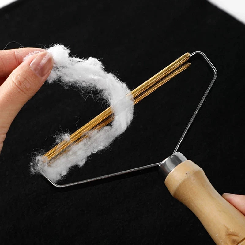 Portable fabric lint remover with a wooden handle and brass head, removing white lint from black fabric.