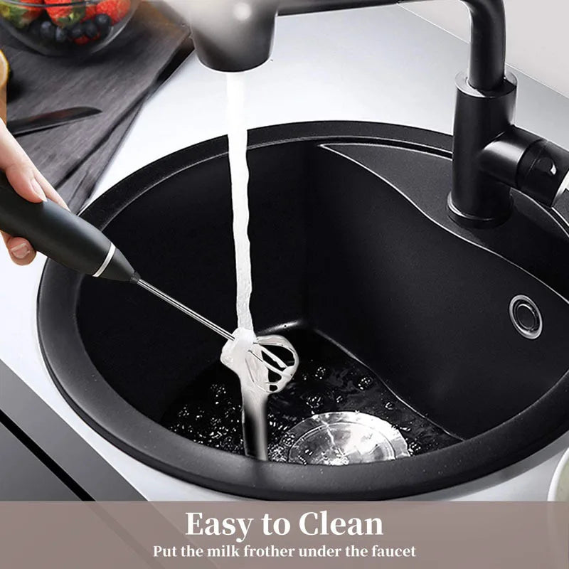 Handheld black electric milk frother being rinsed under a kitchen faucet.