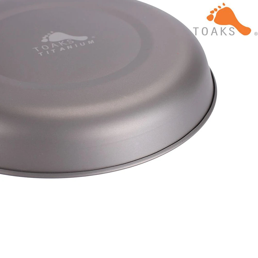 Bottom view of a grey Toaks titanium pan with "Toaks Titanium" printed on it, and the Toaks logo in the corner.