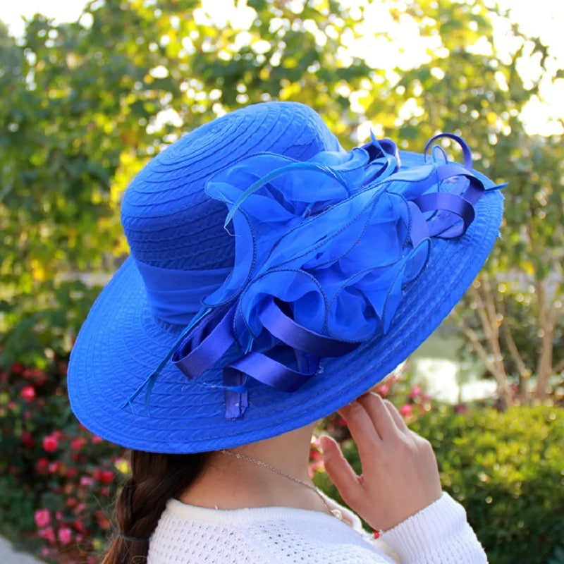 A royal blue, wide-brim occasion hat featuring elegant layered organza flower detailing and a satin ribbon band.