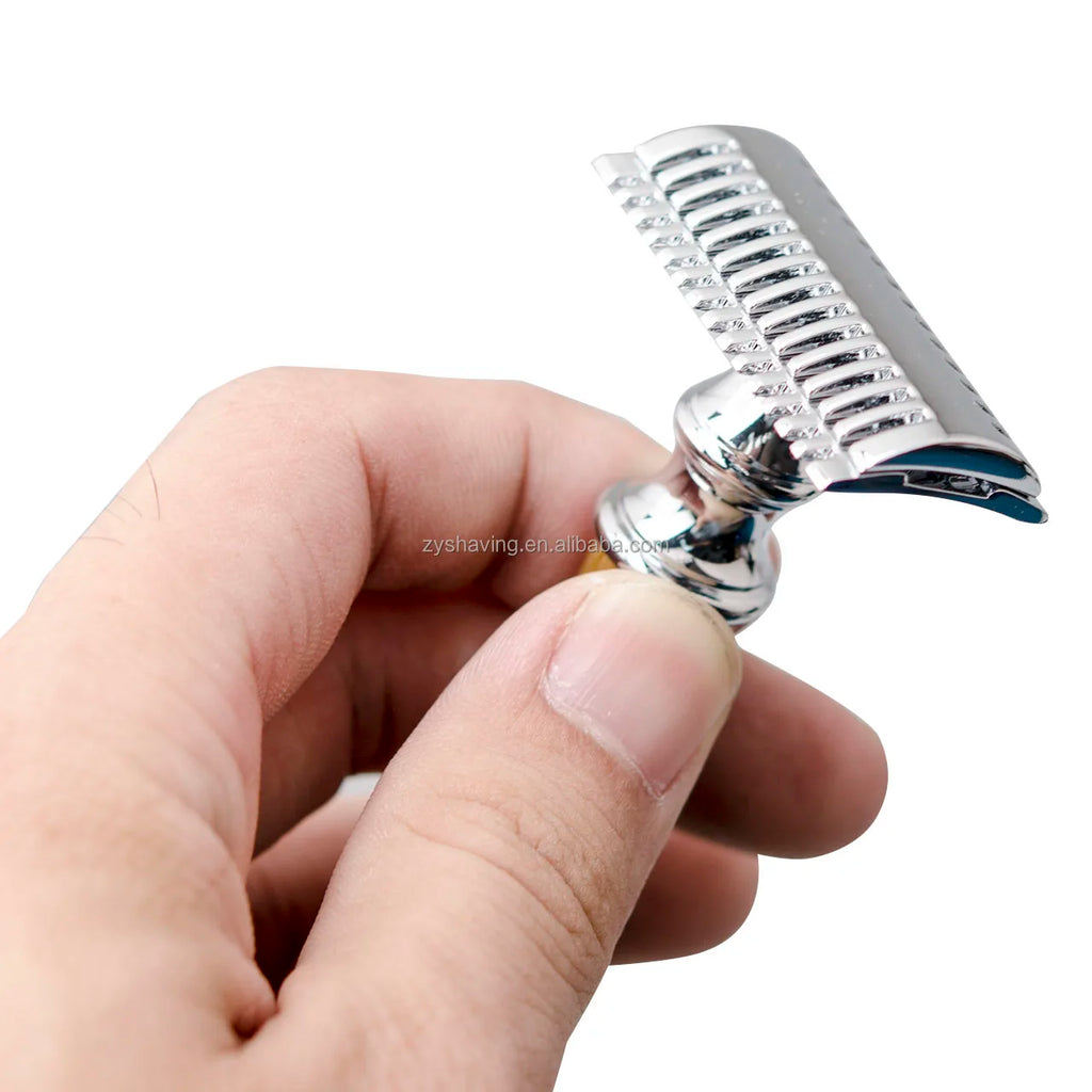 Close-up of a hand holding a luxury safety razor with a shiny chrome finish and a textured open-comb blade guard.