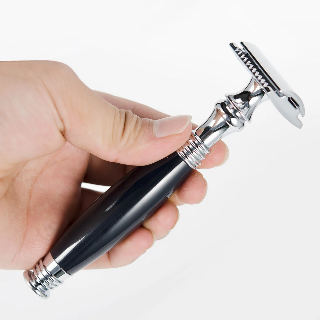 A hand holding a traditional double-edged safety razor with a shiny chrome head and a sleek black handle.