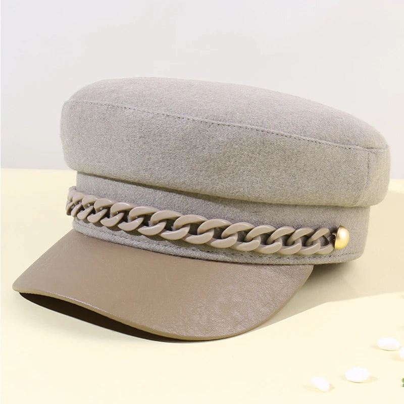 Beige felt baker boy hat with a faux leather peak and a decorative matching chain trim with gold-tone side studs.