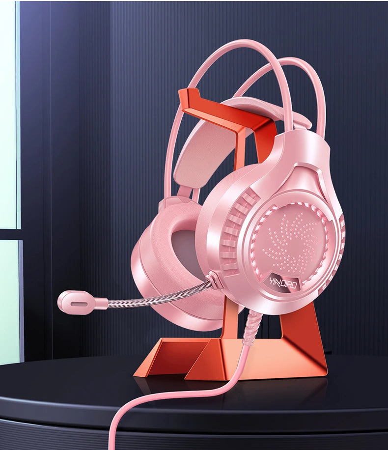 Pink RGB gaming headset with a microphone, displayed on a matching stand, featuring an over-ear design.