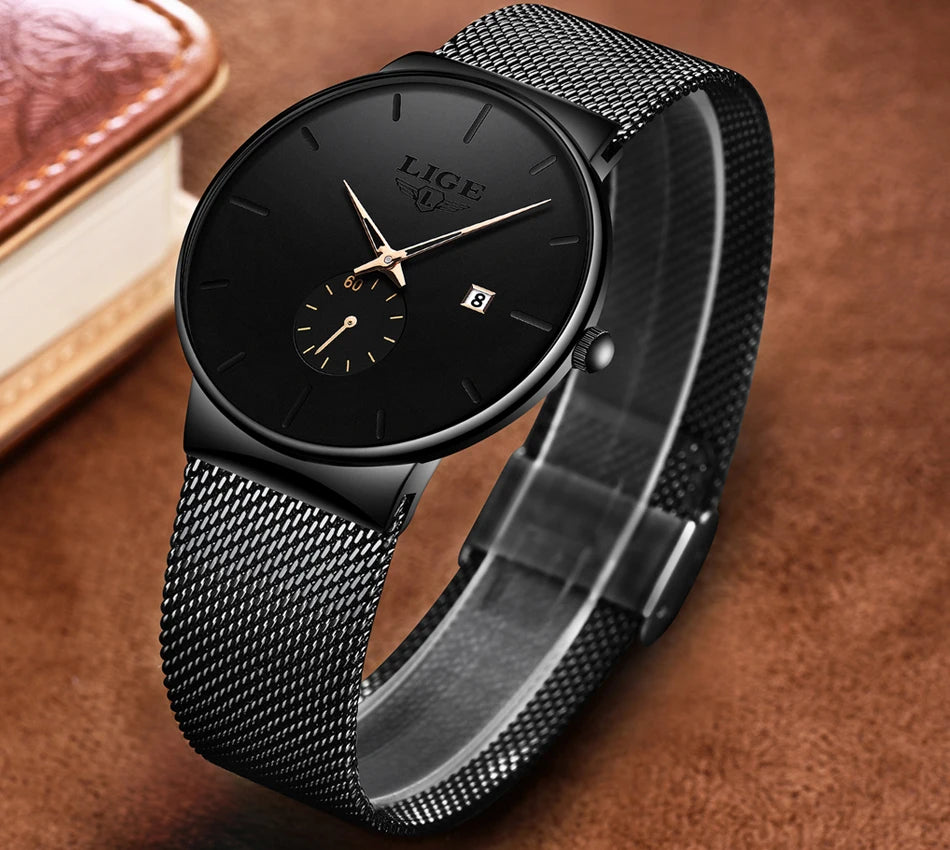 Elegant black ultra-thin watch with a stainless steel mesh strap, gold-tone hands, and a date display.