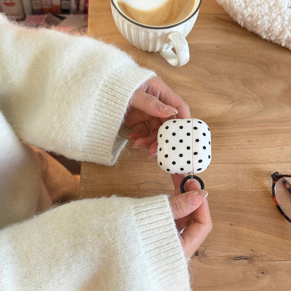 White polka dot silicone case for AirPods, featuring a black attachment ring, held by person in a cream jumper.