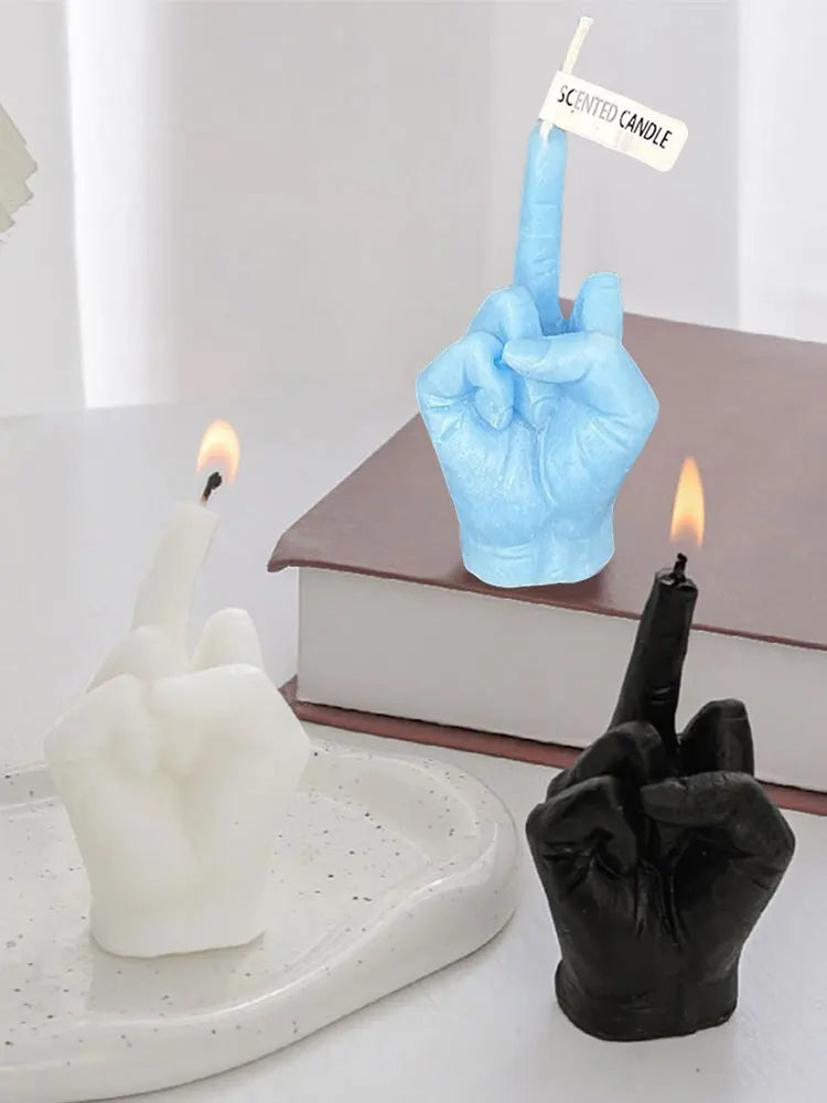Middle finger hand gesture candles in blue, white, and black on a white tray, with white and black candles lit.
