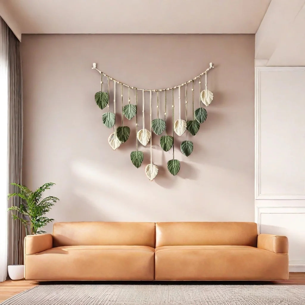 Wall-mounted macrame tapestry featuring cream and sage green leaf-shaped charms hanging in a tiered, arched arrangement.