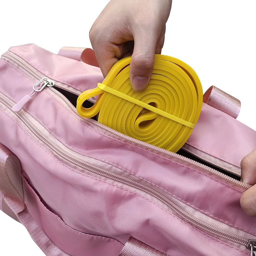 A hand places a rolled yellow resistance band into a pink gym duffel bag.