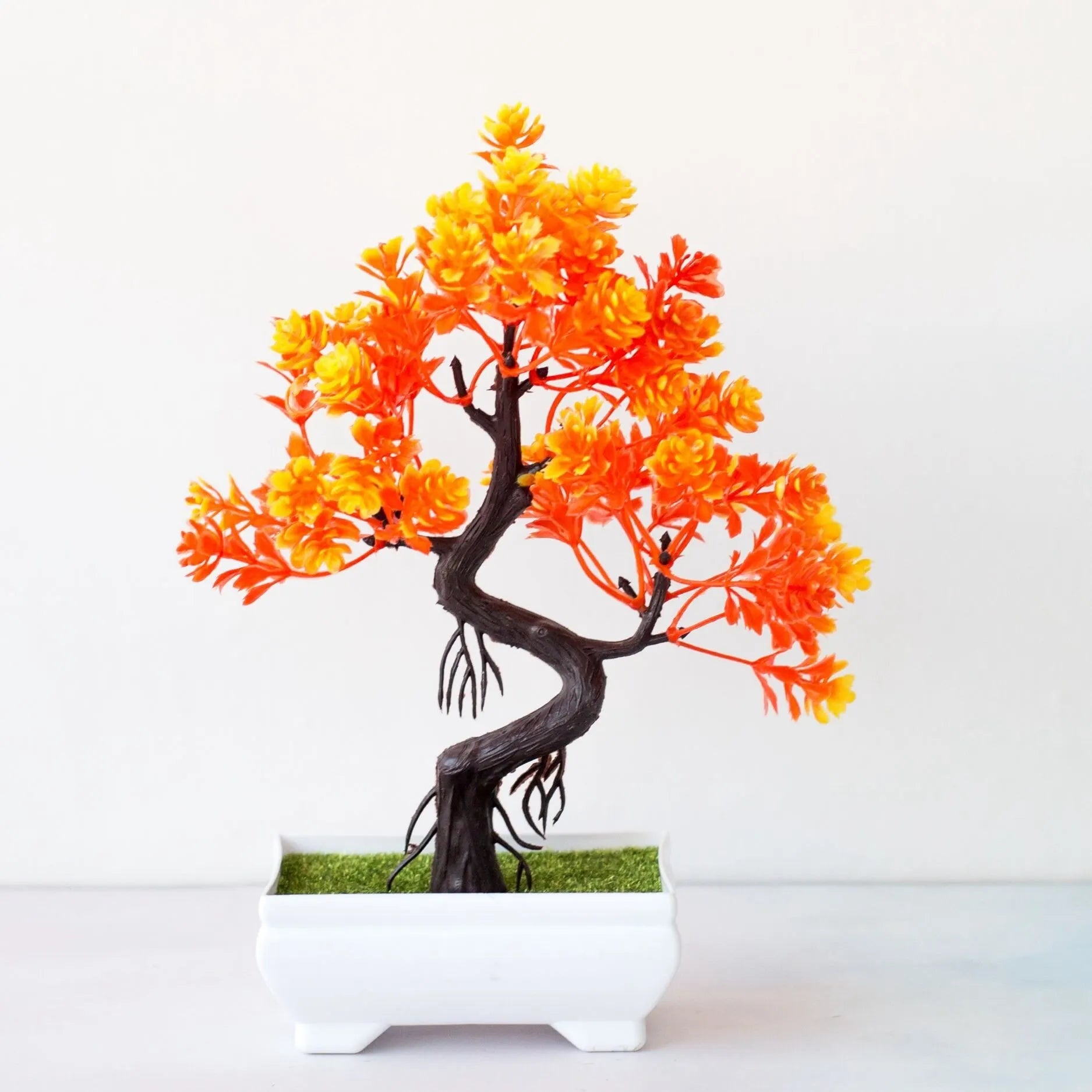 Artificial bonsai tree with vibrant orange and yellow foliage in a small white rectangular pot on a white surface.