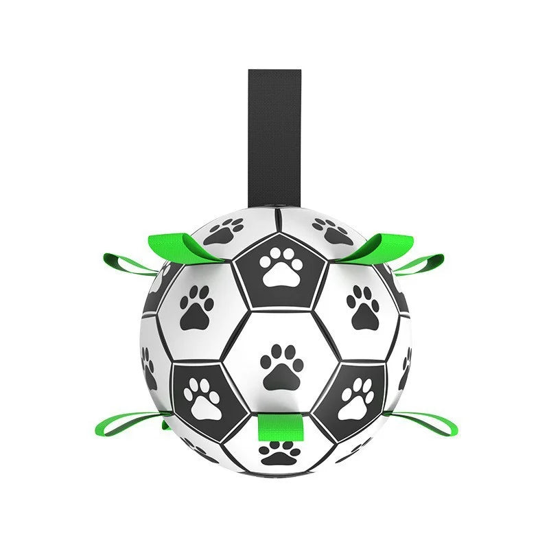 Black and white football-style dog toy with paw print patterns and green nylon grab straps for tugging and fetch.