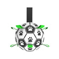 Black and white football-style dog toy with paw print patterns and green nylon grab straps for tugging and fetch.
