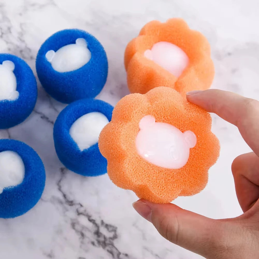 Hand holding an orange flower-shaped sponge with a white bear centre, beside blue bear-shaped sponges on marble.