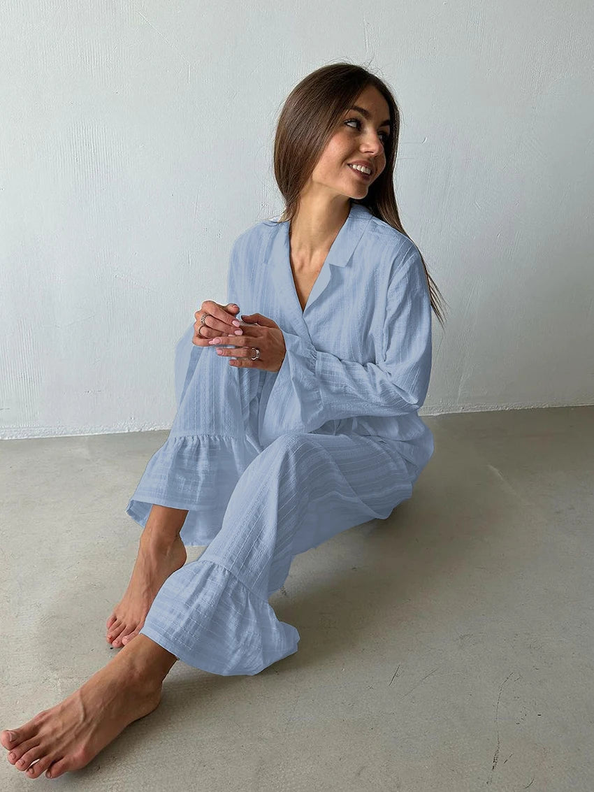 A woman wearing a pale blue textured pyjama set with a collared long-sleeve shirt and frilled-hem trousers.