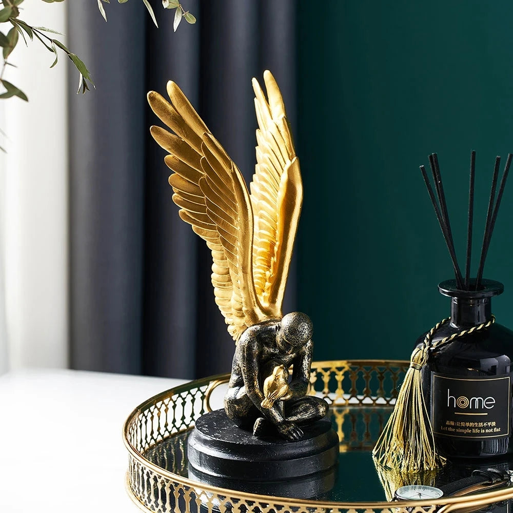 Decorative sculpture of a seated angel with large, detailed gold wings on a round black base.