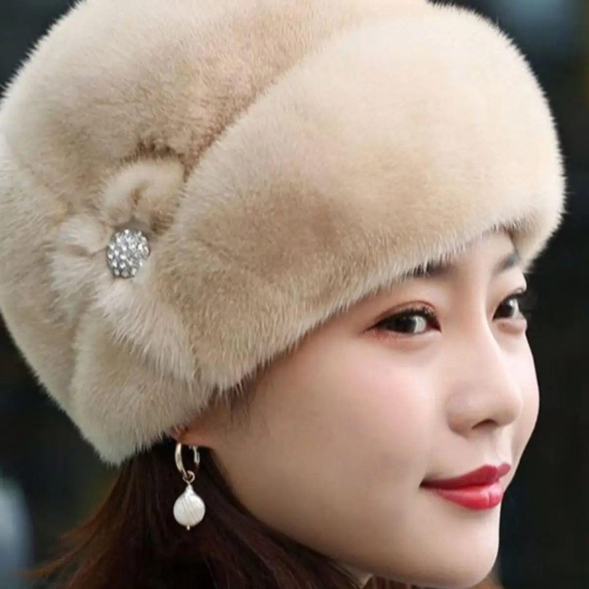 Elegant beige faux fur winter hat with a decorative side embellishment featuring sparkling crystals.
