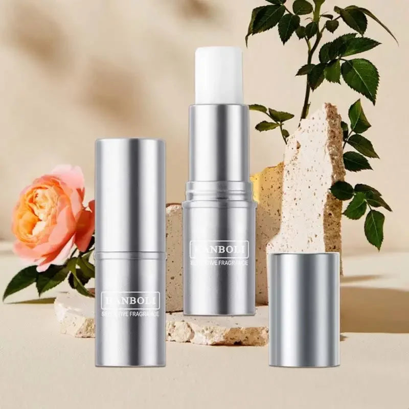 Silver cylindrical solid perfume stick in a metal case with a white applicator on a decorative stone and flower background.
