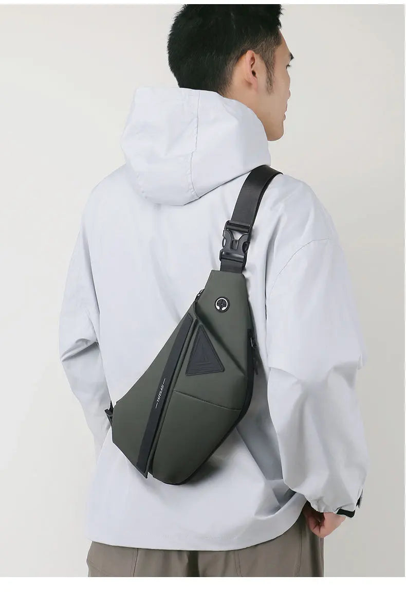 A man wearing an olive green, water-resistant crossbody sling bag with a secure buckle strap and headphone port.