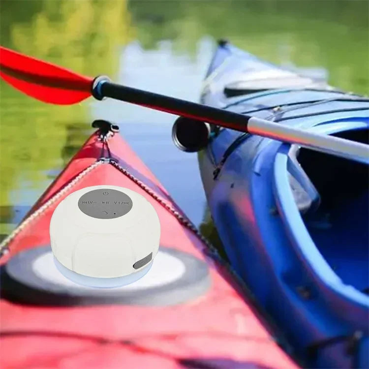 White wireless waterproof Bluetooth speaker with a suction cup, resting on a red kayak on the water.