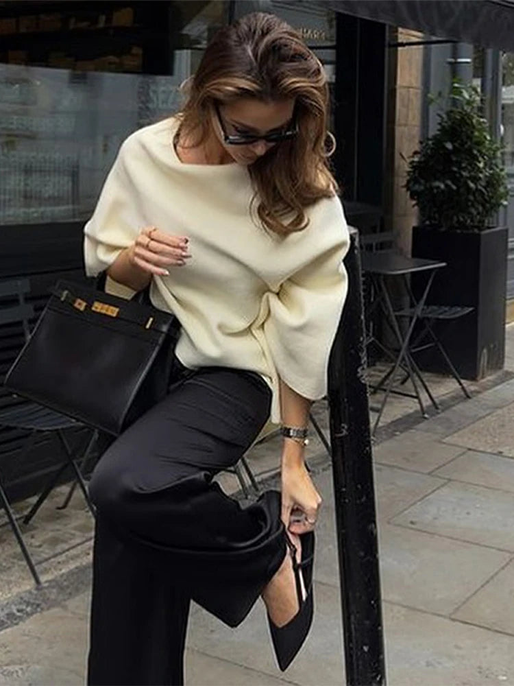 Cream irregular draping knit sweater with wide sleeves, worn with black pants and a black handbag.