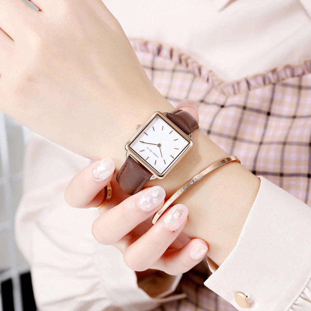 Women's quartz watch with a square gold case, white dial, and brown leather strap on a wrist.