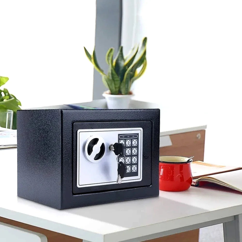 Black metal security safe with a silver electronic keypad and manual key lock sitting on a white desk.