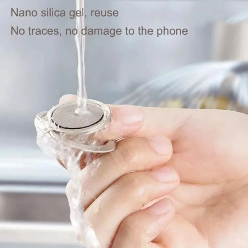 A silver, circular adhesive phone ring holder being washed under running water.