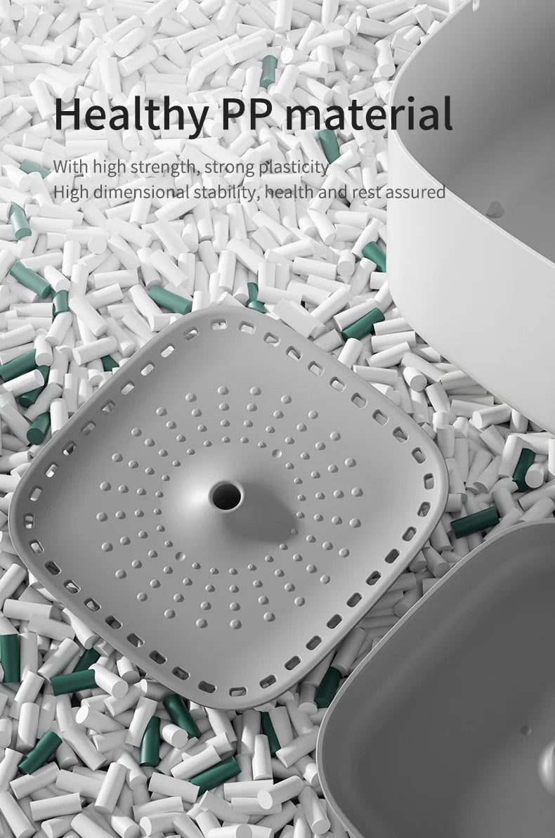 Square grey plastic sink strainer with a central drainage hole and perforated design, set against scattered filler bits.