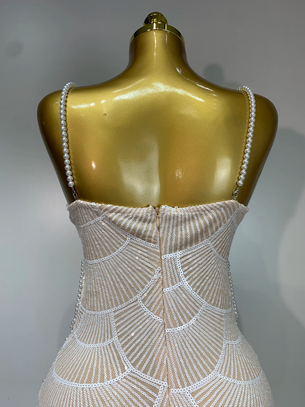 Back view of a nude and white sequined bodycon evening dress featuring pearl-beaded straps on a gold mannequin.