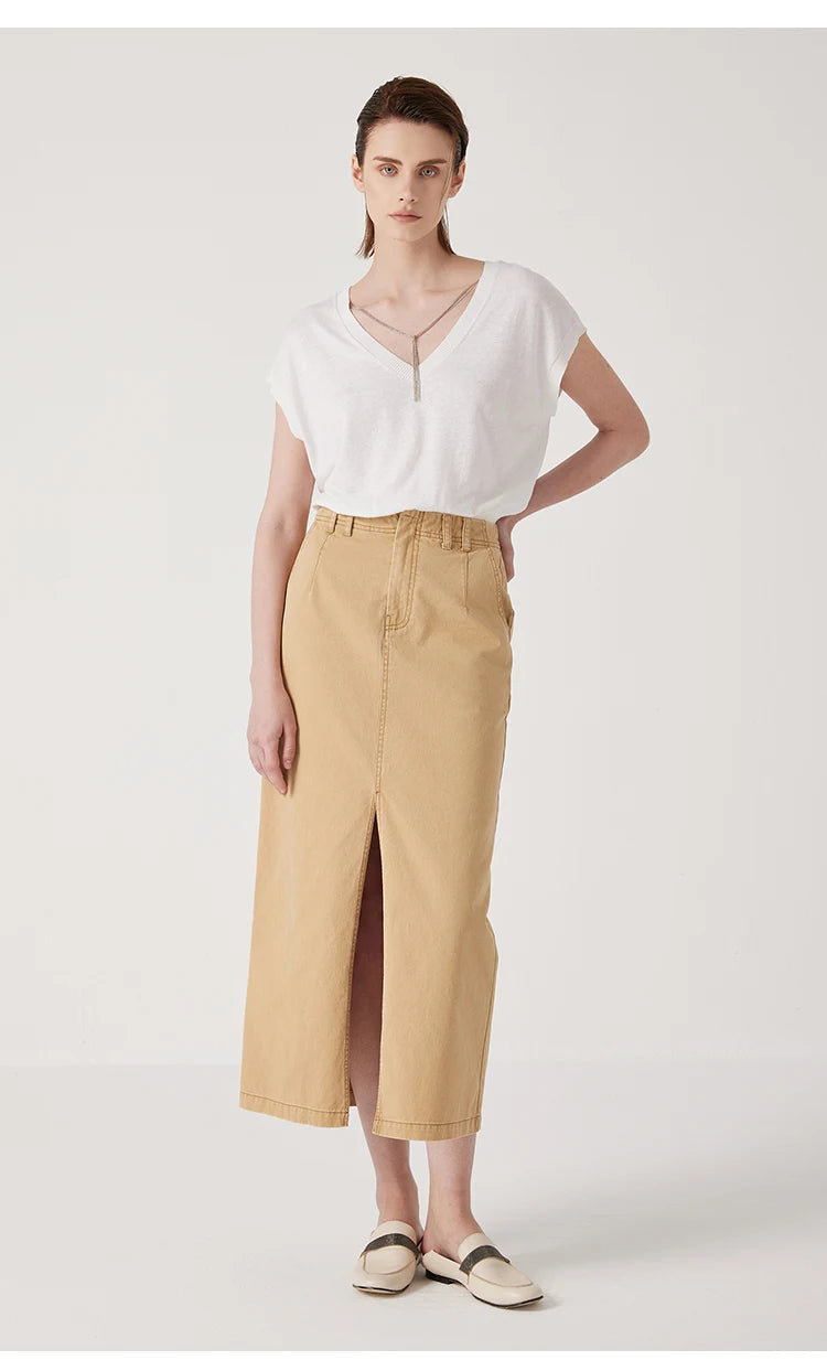 Model wears a high-waisted, tan midi skirt in sturdy cotton with a front slit, paired with a white V-neck top.